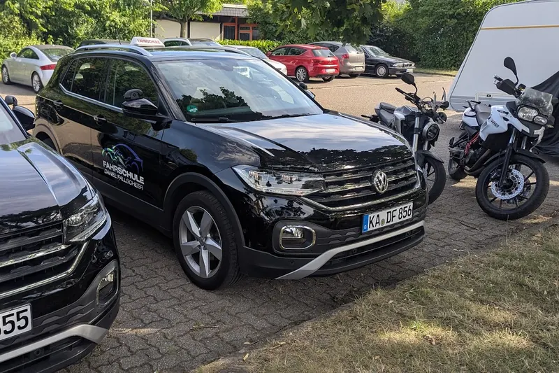 Fahrschulauto – ein schwarzer VW T-Cross mit Fahrschul-Schild auf dem Dach, daneben zwei Motorräder